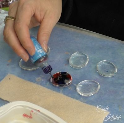 Blue alcohol ink being dripped onto the glass gem and blending with the red ink.