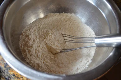Lemon Zest sugar mixed with flour, baking powder, baking soda, and salt with a whisk in a medium sized stainless steel bowl.