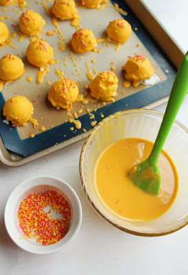 These super fun orange creamsicle ice cream bon bons only take 4 ingredients (including the sprinkles!) and a few minutes to make. They are a perfectly easy and delicious summer treat! bowl of orange magic shell, bowl of sprinkles and tray of dipped orange creme bon bons