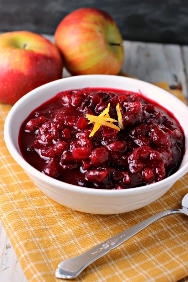 Apple Cranberry Sauce | by Renee's Kitchen Adventures in a white bowl garnished with orange zest and apples in the background