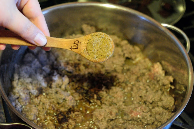 Cumin being added to the cooked ground beef in the skillet. 