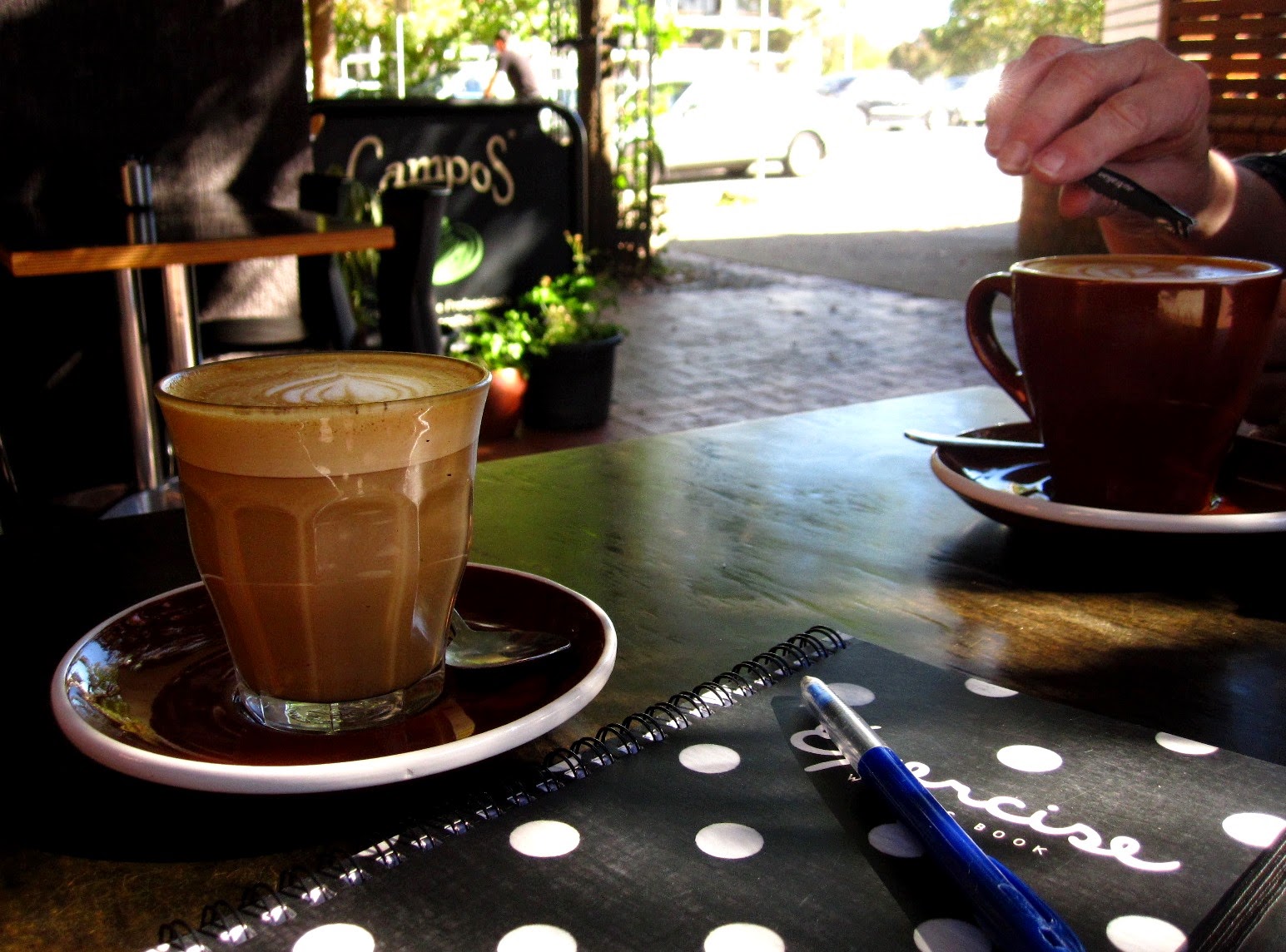 Two cups of coffee and a notebook on an outdoor cafe table.