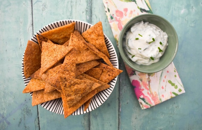 A bowl of tortilla chips next to a smaller bowl of lemon and chive dip