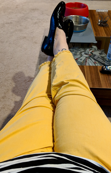 image of my body from the waist down with my feet up on the coffee table; the image shows the bottom of a black and white striped top, yellow jeans with freyed cuffs, and shiny black loafers