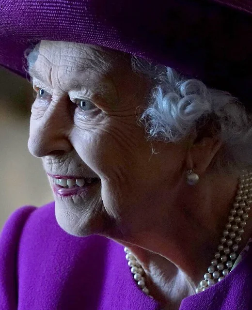 The Queen wore a floral print dress and purple coat and purple hat. diamond brooch