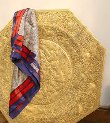 An octagonal brass tray table with a red, blue and brown 1960s silk scarf draped over it