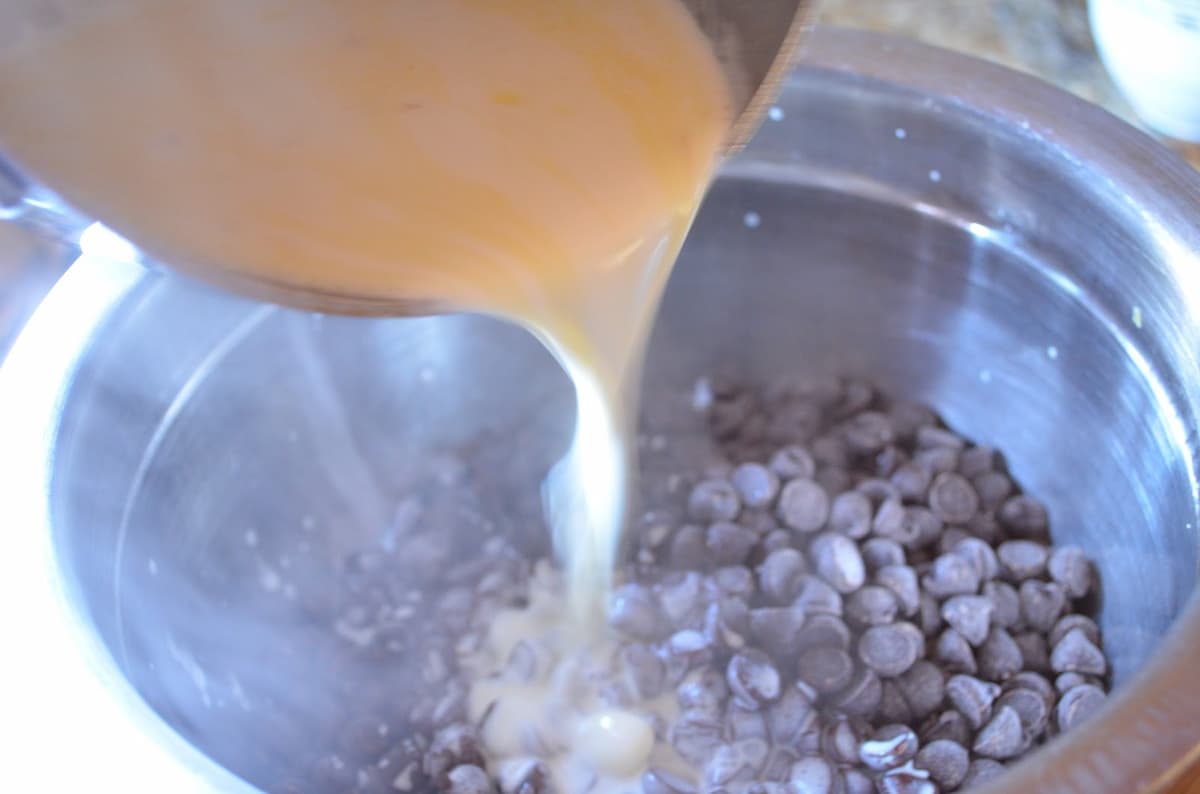 Hot Cream mixture being poured over chocolate chips in a stainless steel mixing bowl.