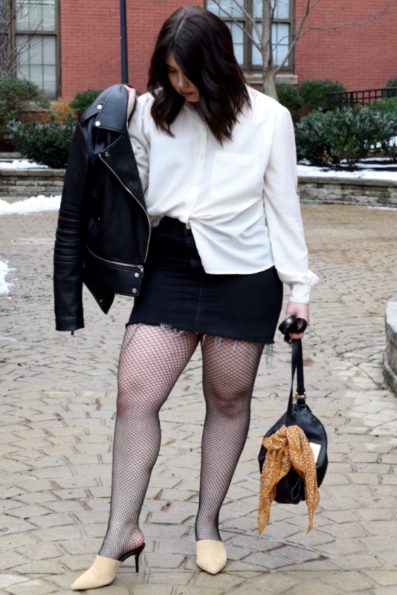 Plus size woman wearing a black mini skirt, black fishnets tights and mules