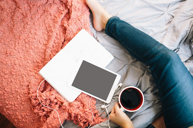 Girl on floor with laptop,tablet,earbuds,cup of coffee and blanket  