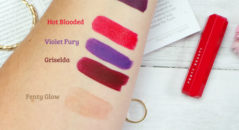 Swatches of lipstick on an arm. Top to bottom is Hot blooded/red, violet fury/purple, Griselda/burgundy, Fenty Glow/nude gloss