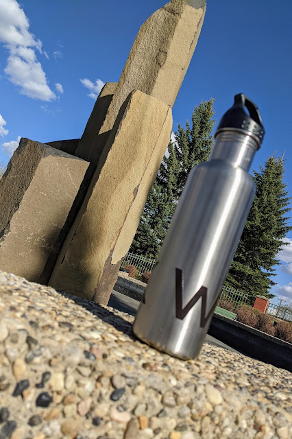 A worm's eye view of the custom walk stainless steel water bottle in front of a few large sculpted rocks. It's a nice sunny day.