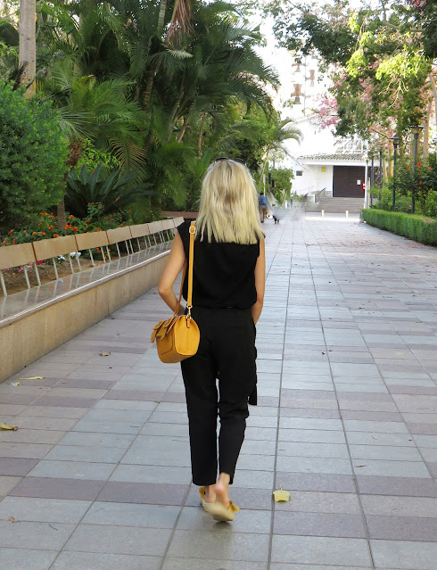 Alejandra Colomera con camiseta negra, pantalón formal negro, lazo en el cuello negro con lunares blancos y complementos mostaza