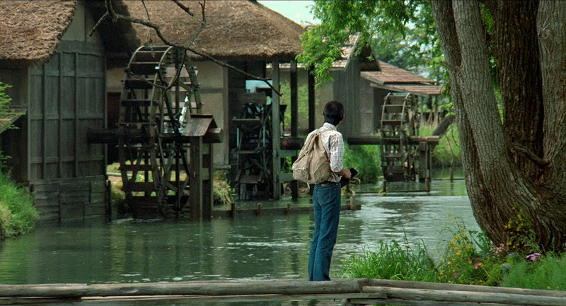 Man in foreground looks back at a series of watermills