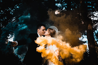 Pareja de novios besándose en una foto y sosteniendo antorchas de humo en amarillo y azul