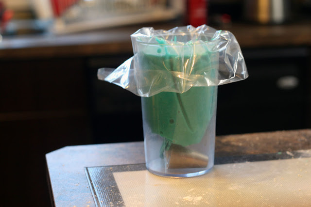 A piping bag filled with the macaron batter sitting inside a large measuring cup.