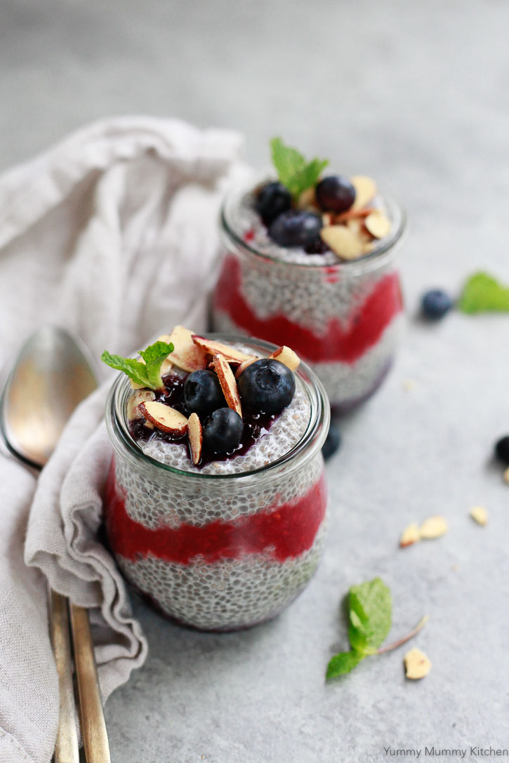 Two glass jars filled with layers of chia pudding and berry sauce topped with fresh blueberries and sliced almonds. 