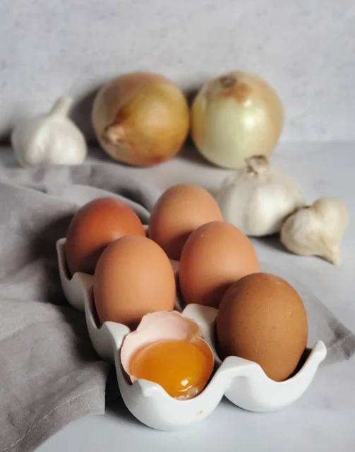 eggs in tray, one cracked egg, onion, garlic