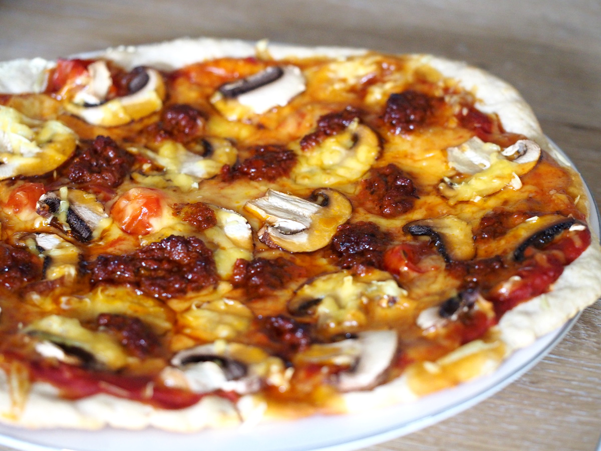 Pizza gebacken mit Sauerteig und belegt mit Pilzen, Käse und Pesto rosso.