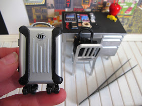 Modern dolls' house miniature suitcase, being held in front of an office scene.