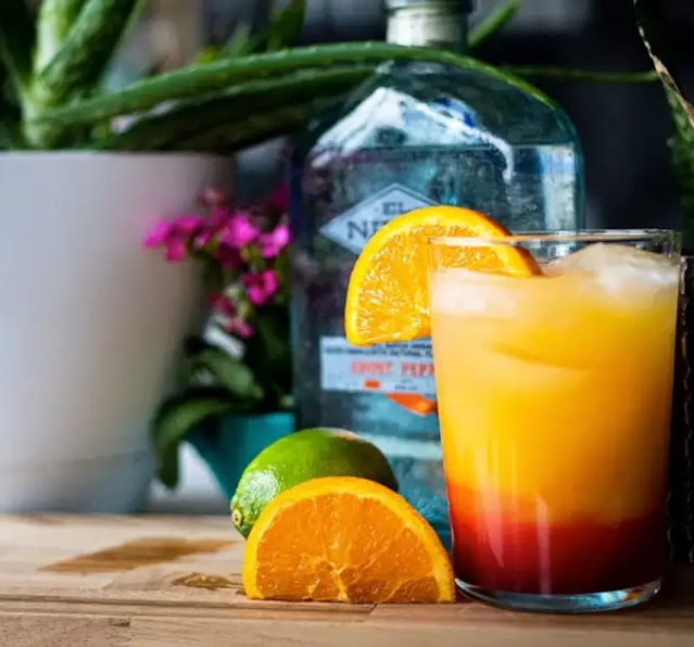 Vaso de cristal con coctel tequila sunrise adornado con una rebanada de naranja, sobre una mesa de madera