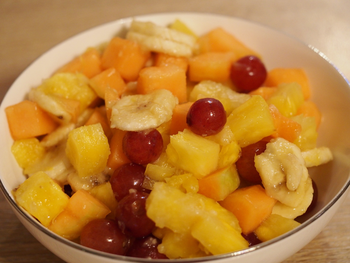 Eine große Portion des Obstsalats aus Ananas, Cantaloupe Melone (mit orangenem Fruchtfleisch), roten Trauben und Bananenscheiben in einer Schüssel