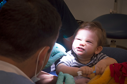 Baby smiling at doctor, holding a tooth brush.