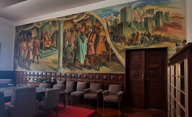 ala com mesa central de reunião e várias cadeiras estofadas, Na parede imensas pinturas históricas
