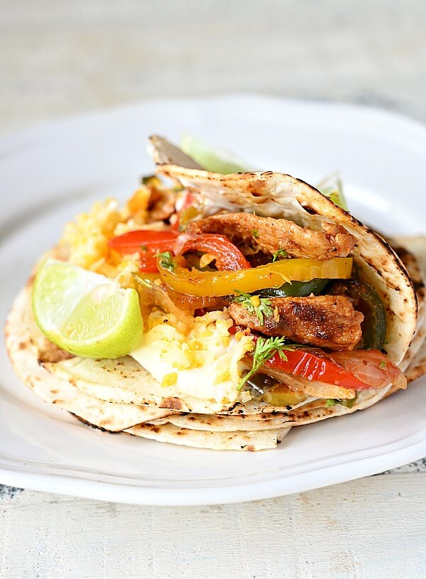 a close up of a white plate with easy chicken fajitas,bell peppers,sour cream and lemon wedges