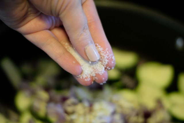 A hand seasoning the zucchini, onion, and garlic, in the pan. 