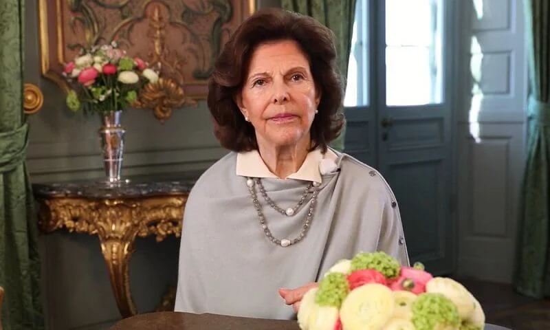 The symposium was organized by Harvard University. Queen Silvia of Sweden wore a gray cape with side buttons. Pearls necklace