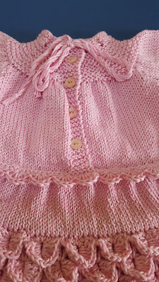 Zrobiona na szydełku różowa sukienka dla malutkiej dziewczynki 