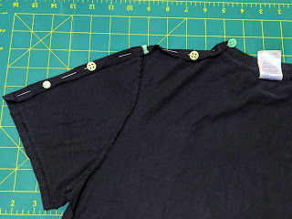 One side of a black tshirt with freshly cut edge pinned, ready to be machine sewn