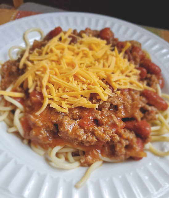 chili topped spaghetti in a white bowl topped with shredded cheddar cheese