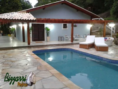 Construção de piscina em alvenaria com o revestimento de azulejo com o piso da piscina com pedra São Tomé sendo tipo cacão com a construção da residência com o pergolado de madeira.