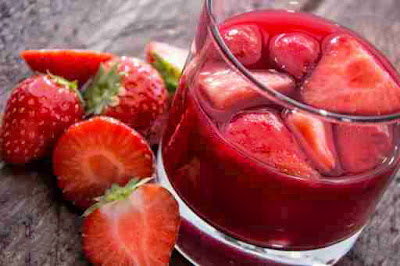 szklanka nalewki truskawek z owocami, a obok przecięte na pol truskawki