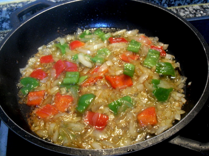 Pochando cebolla y pimientos verde y rojo picados.