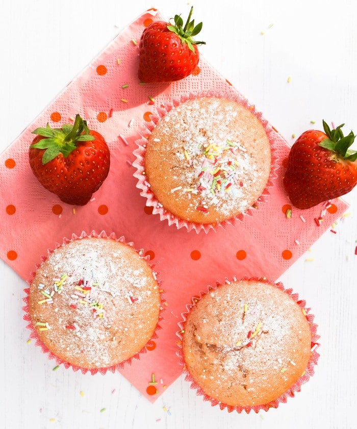 3 strawberry milkshake muffins and 3 ripe strawberries on a spotty pink napkin