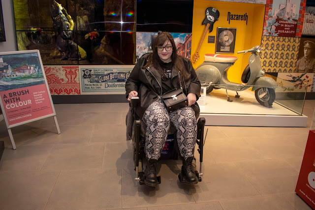 Plus size woman wearing grey snake print leggings, black tee and black jacket, the library in the background