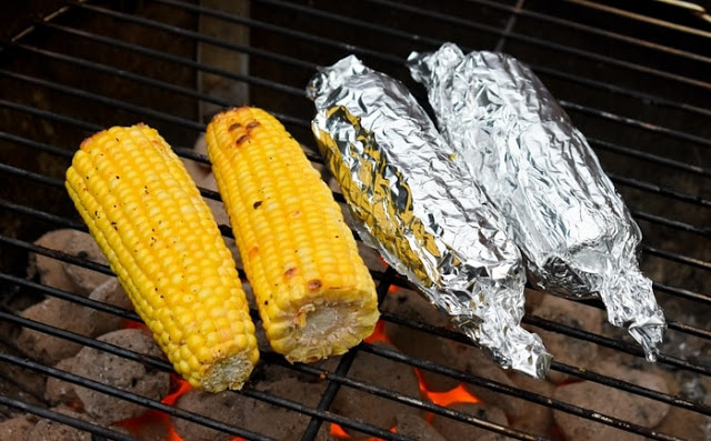 Corn grilling on a BBQ, both foil covered and naked corn cobs.