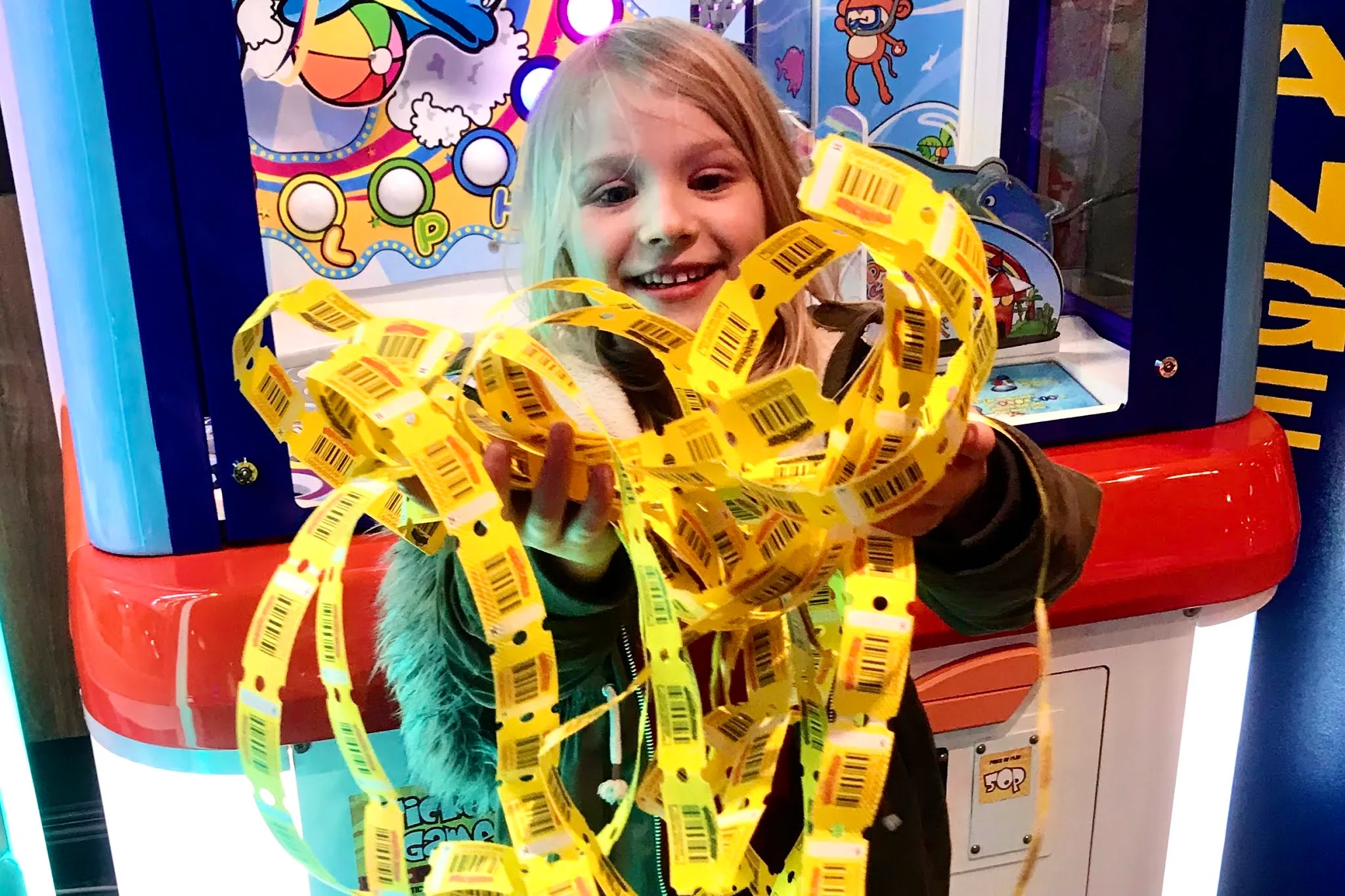 A girl holding an armful of winning tickets from an arcade machine