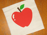 A square of calico with a 3-coloured print of an apple with stalk and leaf.