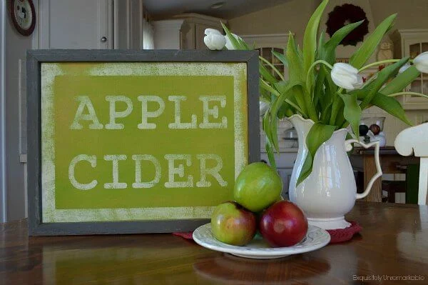 Handmade Green Apple Cider sign in white kitchen with apple and flowers on table.