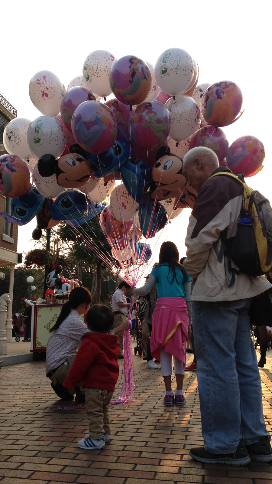 A toddler has fun with balloons at Hong Kong Disneyland. His grandfather would later look at me as I took a second photograph of the kid.