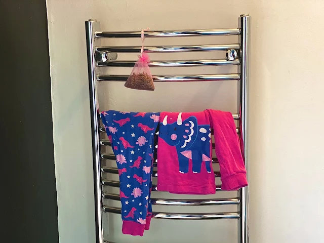 A silver ladder style heated towel rail with Children's Pink Dinosaur Pyjamas warming on them