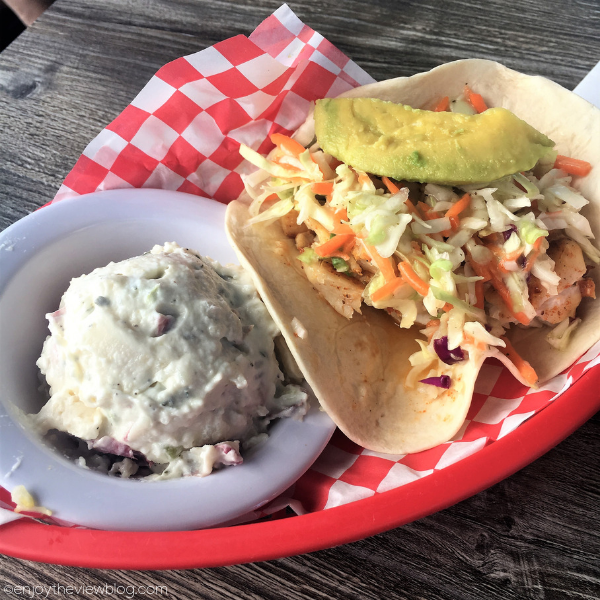 red food basket with two fish tacos and a small bowl of potato salad