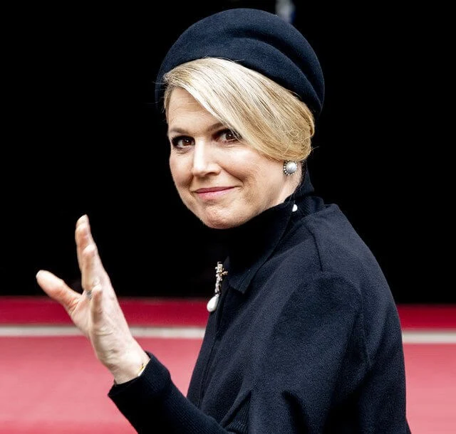 Queen Maxima wore a black wool high collar cape coat. Black leather handbag. Pearl drop earrings and diamond brooch. Gripoix earrings