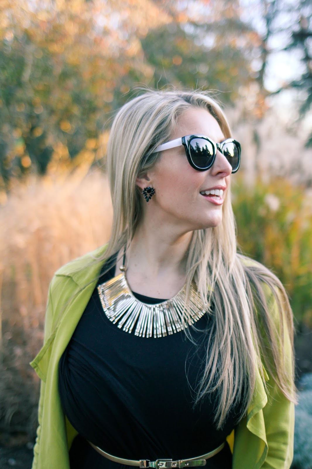 The Goldfields Girl styling maternity fashion. She wears black maternity dress, green jacket, statement gold necklace, brown boots and Michael Kors bag.