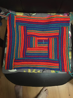 The piece has a mildy rectangular shape with the partially finished strip on the left side of the square portion. The multicoloured stripes of the work are very playful and a bit reminiscent of children's toy blocks.
