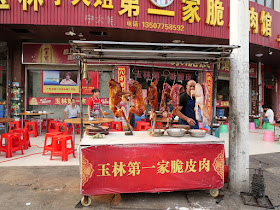 cooked dogs hanging at an outdoor carving table at Yulin's First Crispy Skin Meat Restaurant