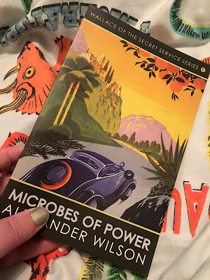 A hand holding a copy of Microbes Of Power by Alexander Wilson